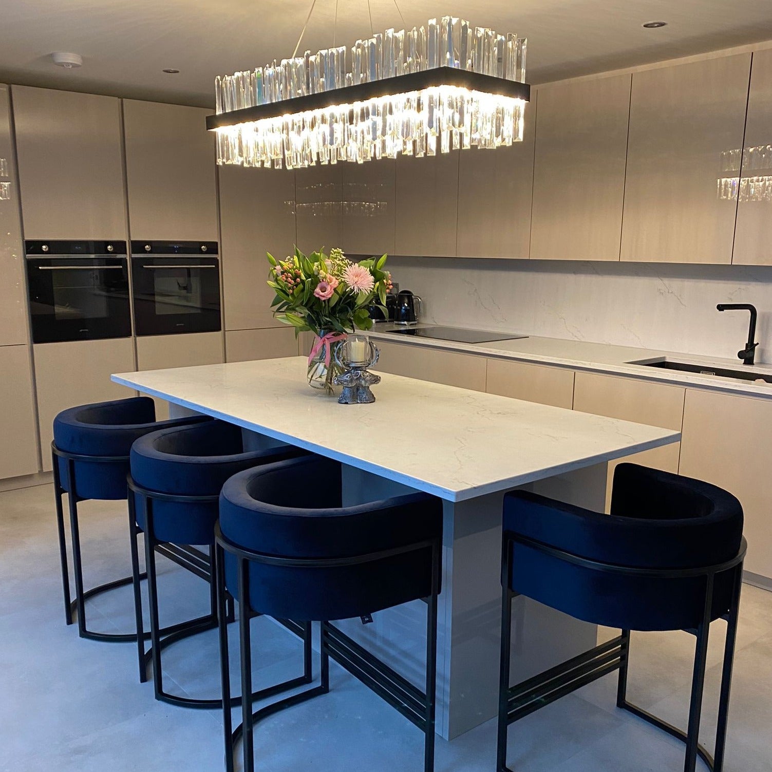 Linear crystal bar chandelier installed above a spacious modern kitchen island in a refined interior