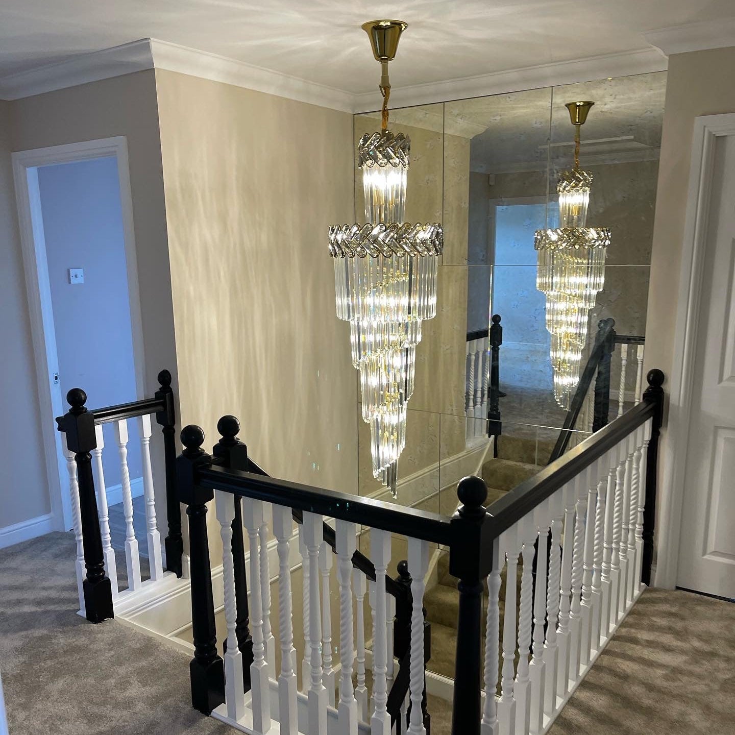 Long spiral stairwell chandelier design with cascading crystal tiers in a high-ceiling residential hallway