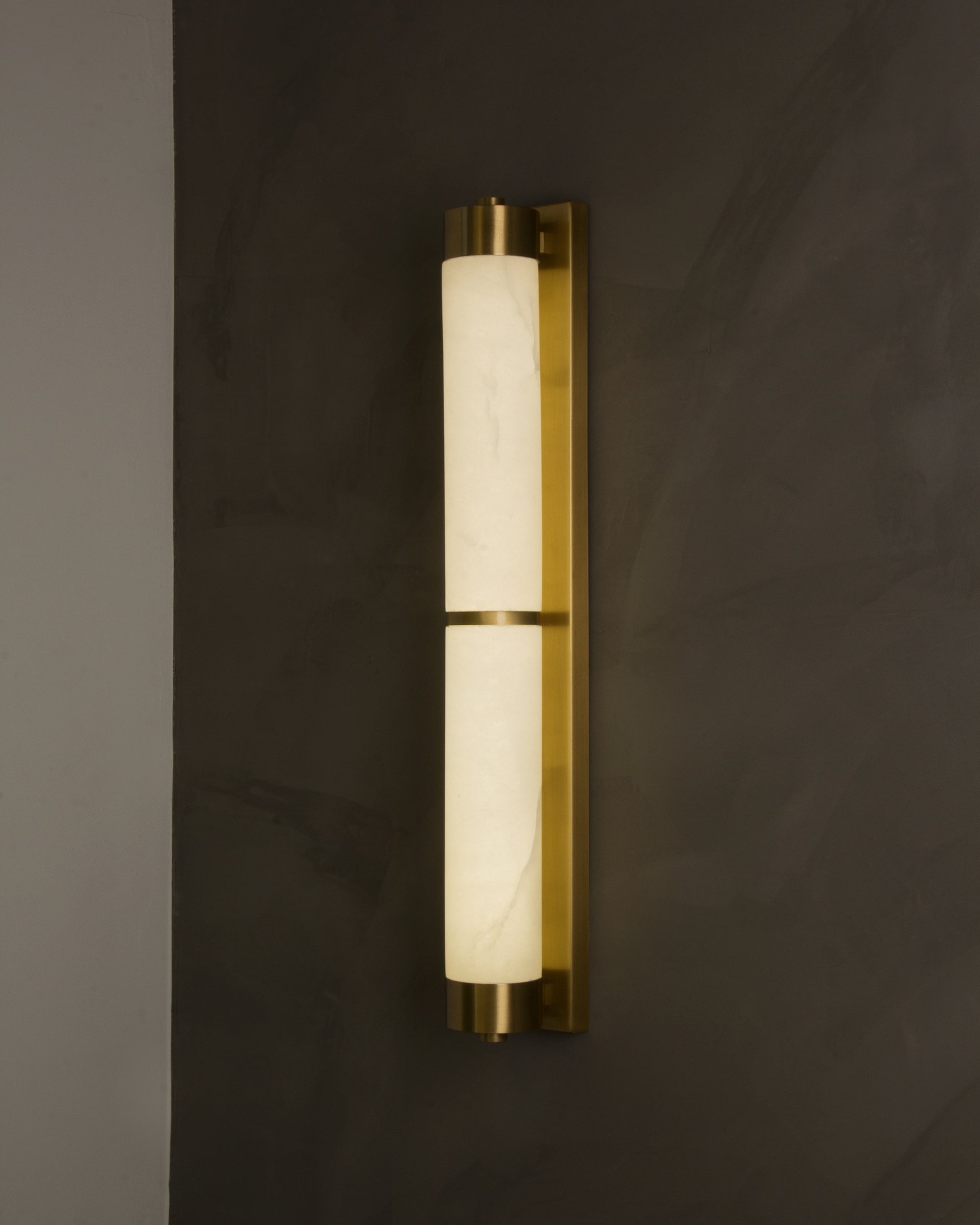 Lucente marble wall light with cylindrical illuminated marble and gold frame mounted on a luxury interior wall