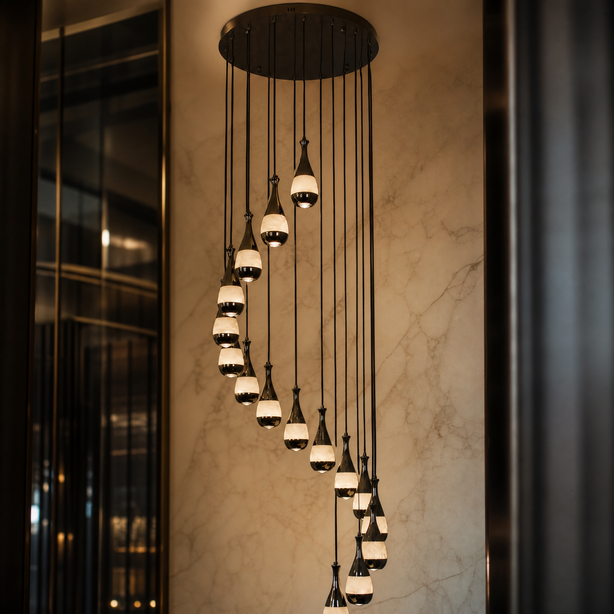 The dramatic spiral silhouette of the VORELLI Armonia marble chandelier, casting a sophisticated and luxurious glow across a multi-story staircase.