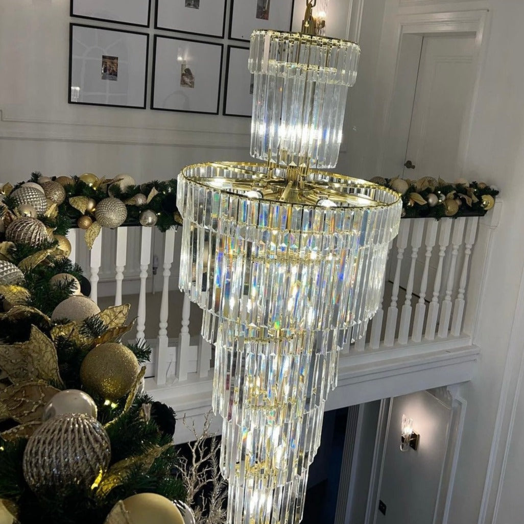 Luxury spiral staircase chandelier with cascading diamond-cut crystal tiers in a double-height interior.