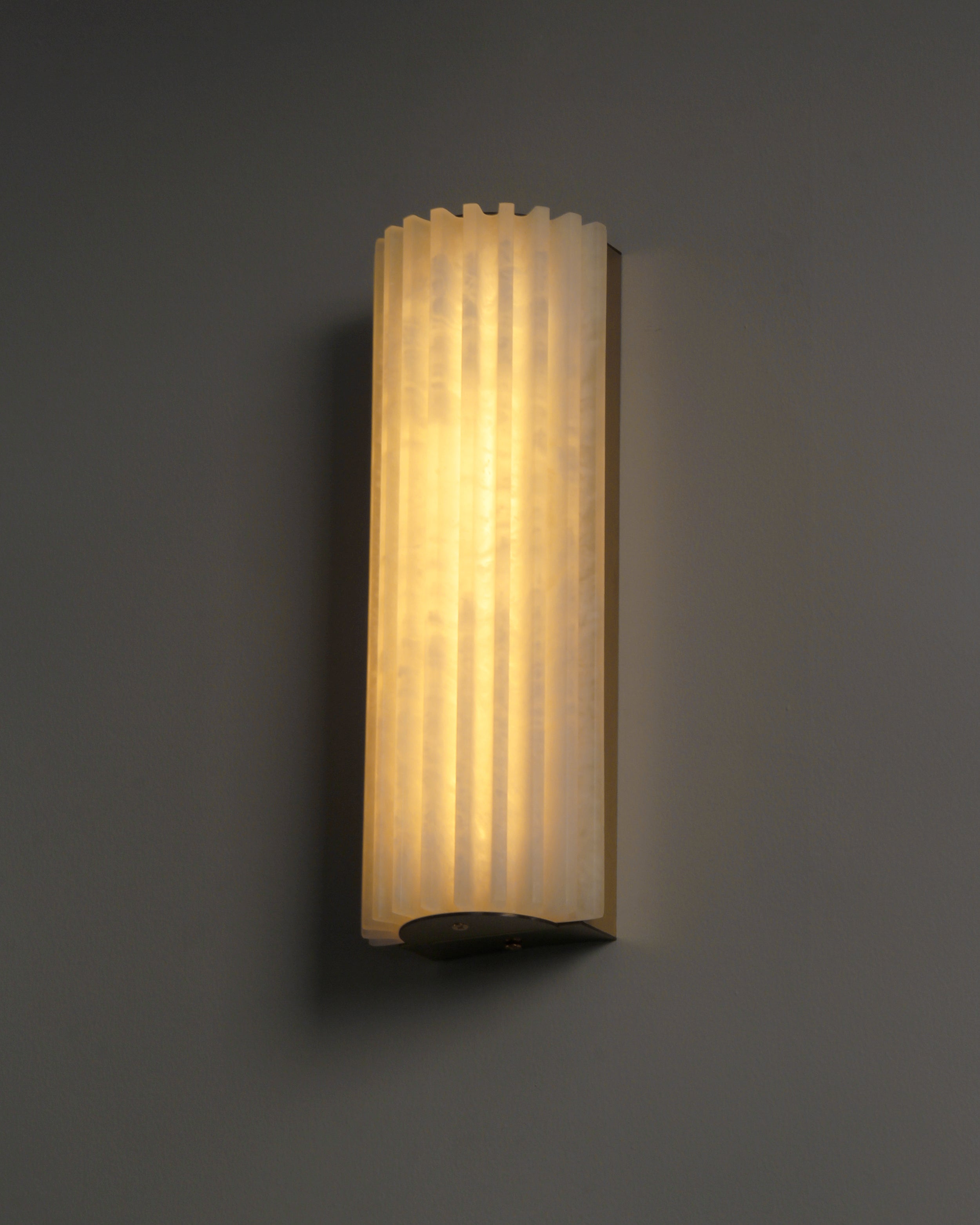 Angled view of illuminated fluted marble wall light showing sculptural depth