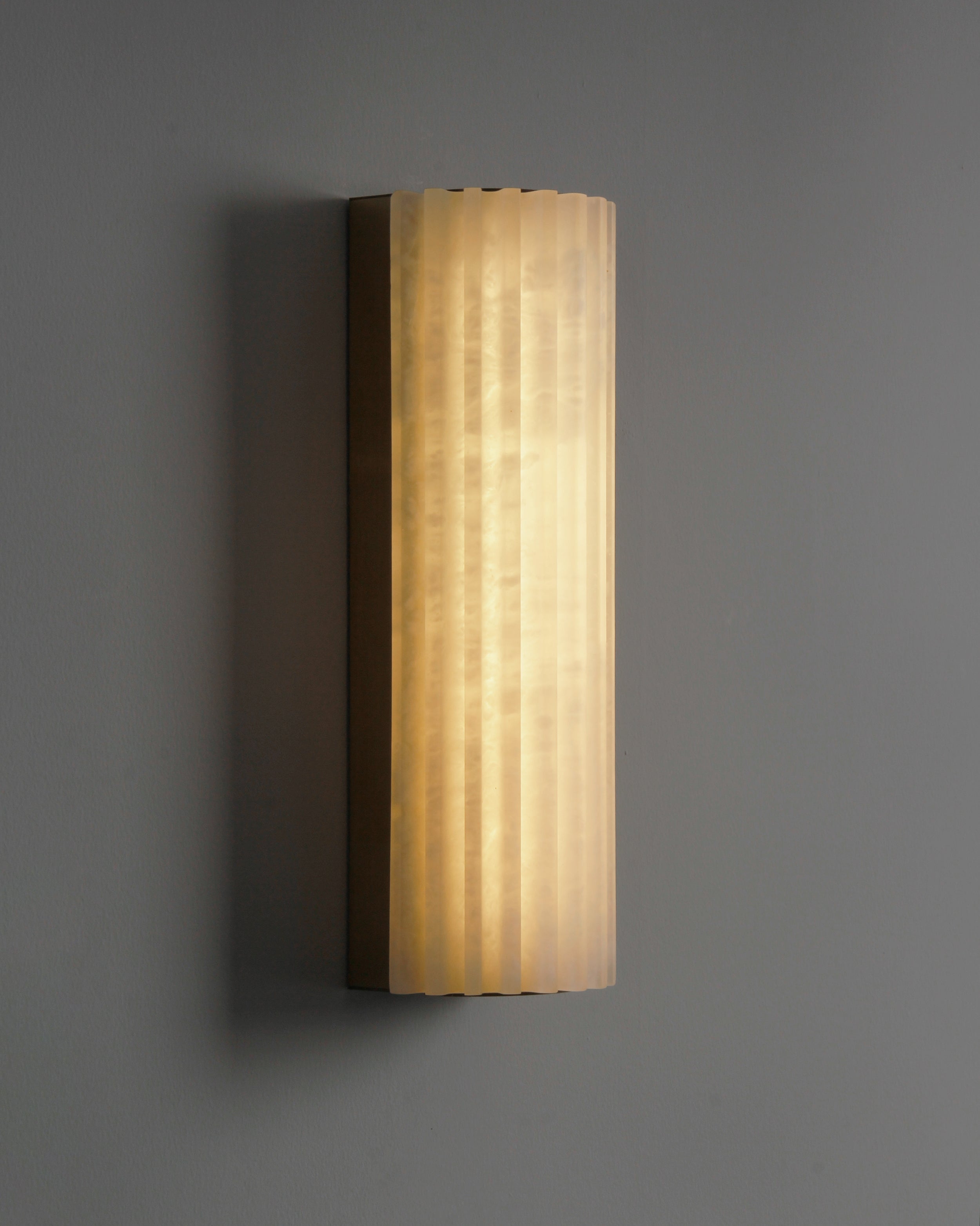 Front view of fluted marble wall sconce with soft diffused glow
