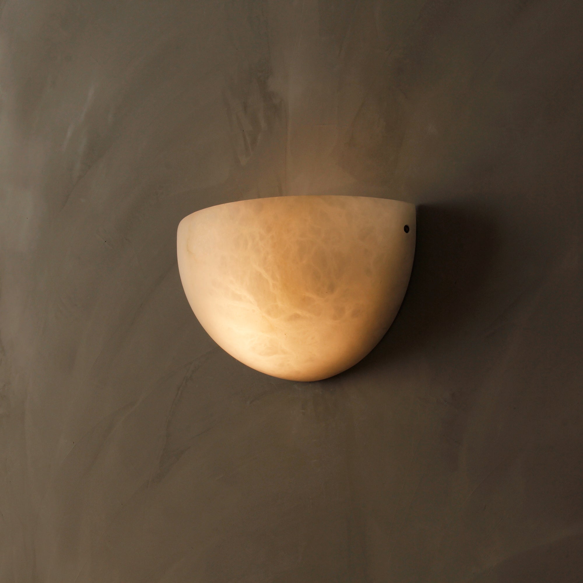 Belluno natural stone wall sconce casting warm ambient light on textured wall