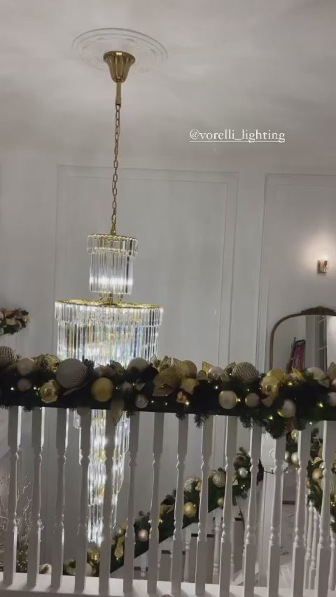 Elegant spiral staircase chandelier with layered crystal drops in a luxury residential interior.