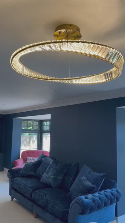 Elegant VORELLI Melia circular crystal chandelier illuminating a contemporary living room interior