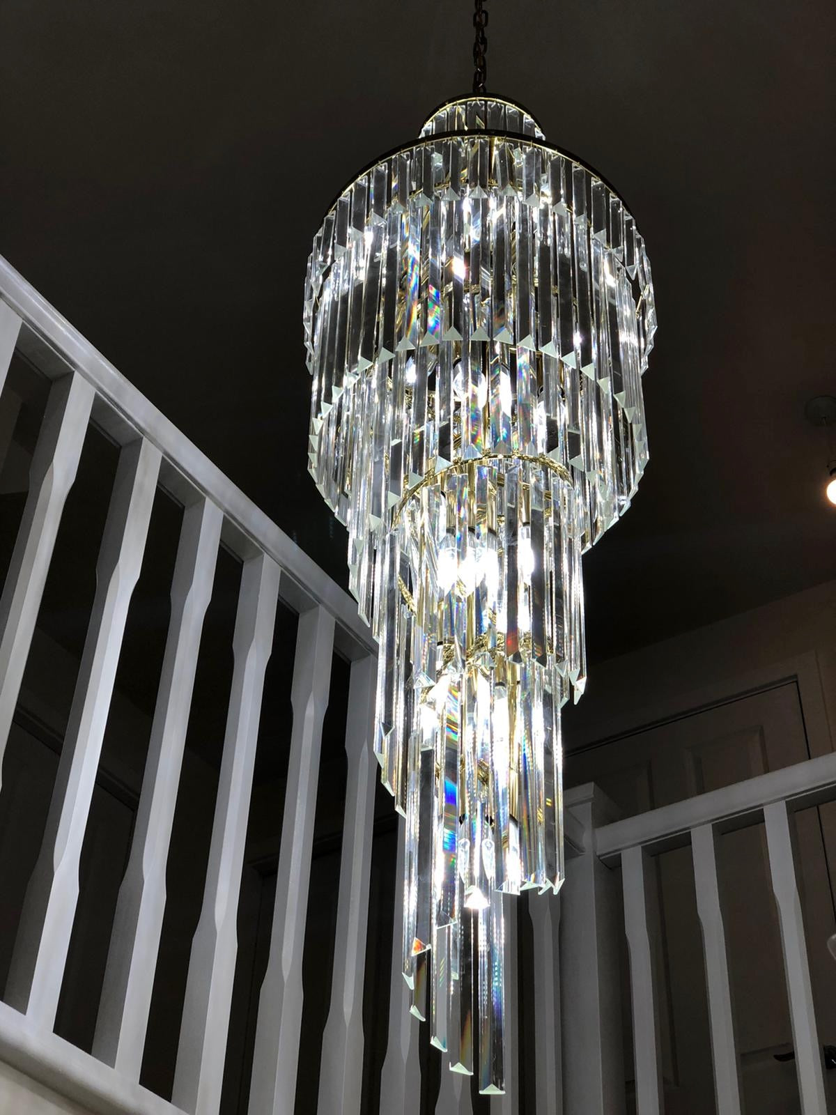 Long spiral crystal chandelier suspended through a tall staircase void with natural daylight.